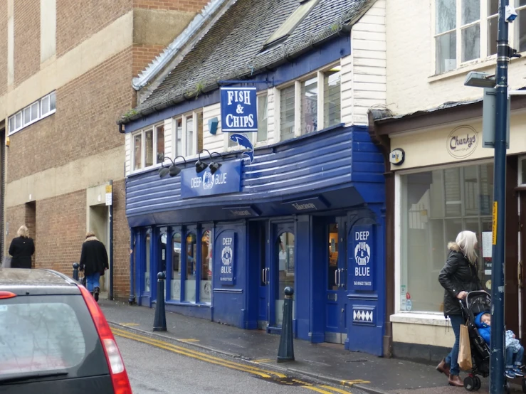 the corner of a city street with shops, businesses and a lady walking down the side walk