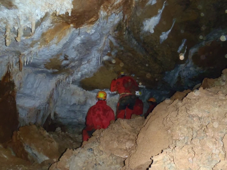 three men wearing red helmets in an underground cave