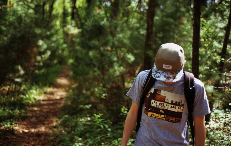 a man wearing a hat and carrying a backpack walks through the woods