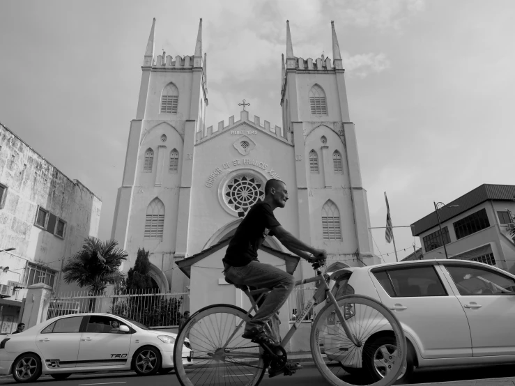 a man on a bicycle passing a car in front of an ornate church