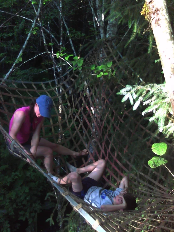 two men hanging in a rope hammock surrounded by trees