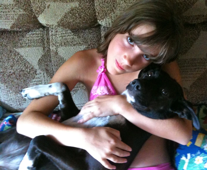 a child in pink swimsuit hugging two dogs on couch