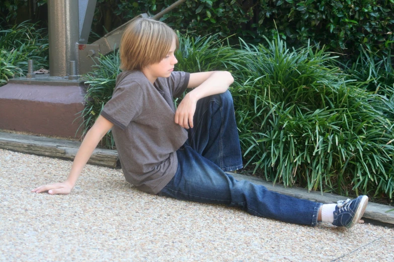 a boy in jeans is sitting on the sidewalk