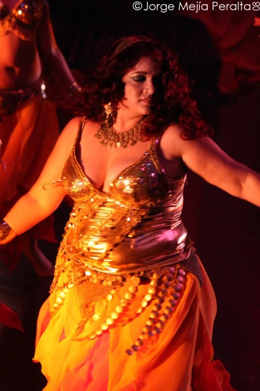 a woman wearing an orange and gold costume performing a belly dance