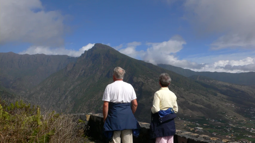 two older people standing on top of a mountain looking into the sky