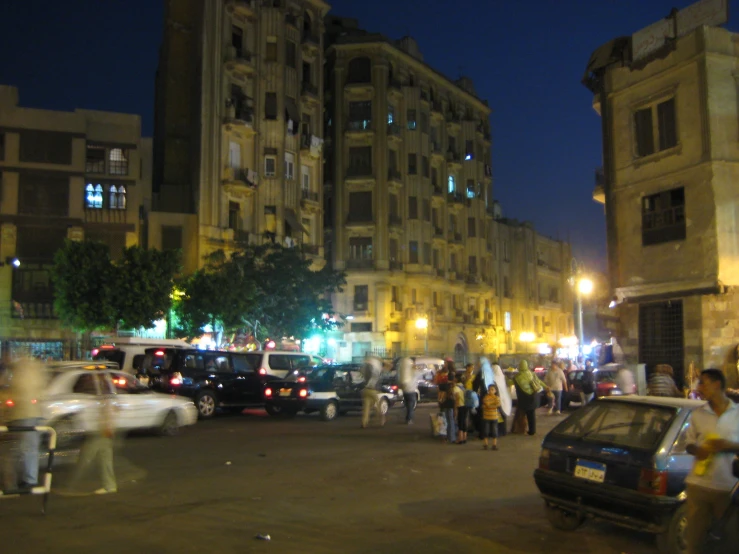 a city at night with lots of parked cars and people