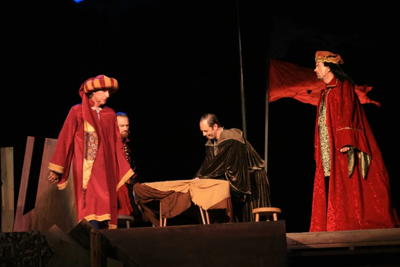 a woman sitting in front of a table next to three men in medieval costumes