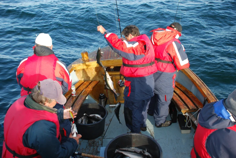 five people standing on a boat fishing in the ocean