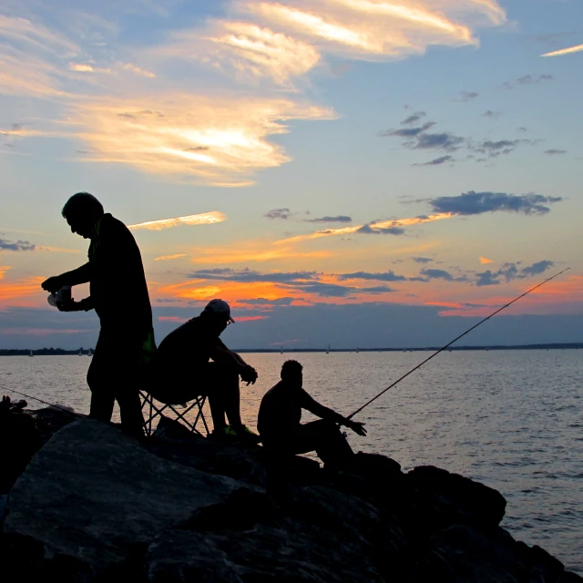 several people in silhouette standing near the ocean fishing