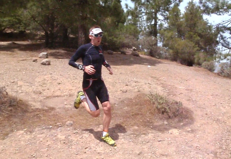 a man running across a dirt field with a forest in the background