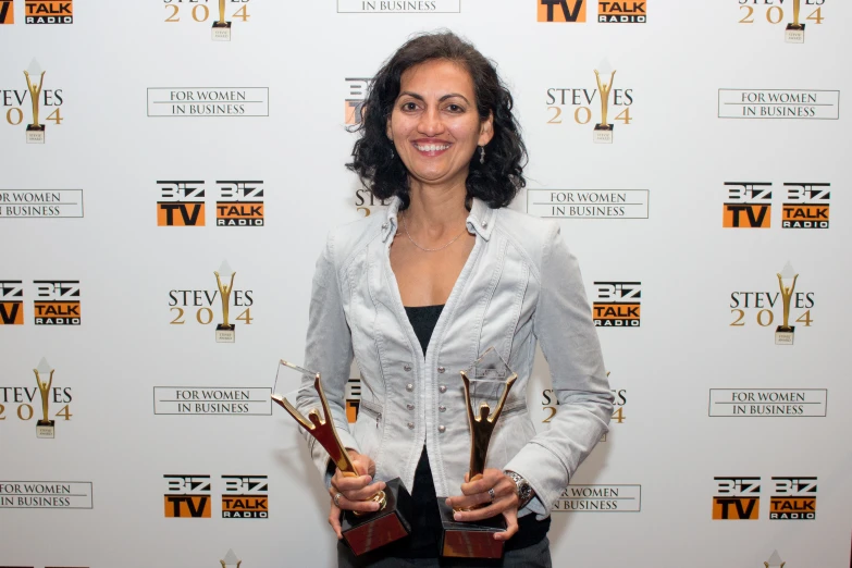 a woman in a blazer and jeans holding two awards
