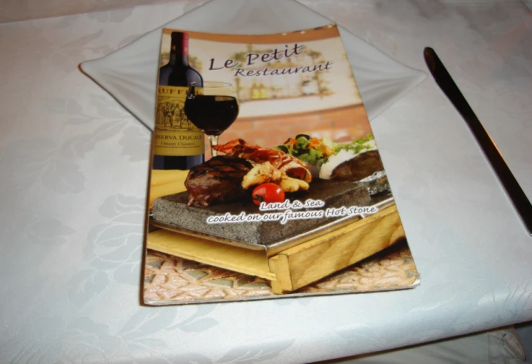 the book titled le petite grandaire is on a table next to a spoon and wine glass