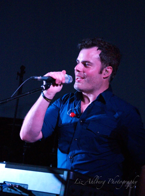 man in blue shirt standing at microphone in front of screen