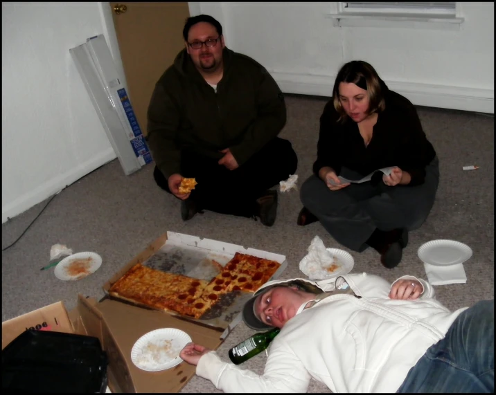 some people are sitting and eating pizza on the floor