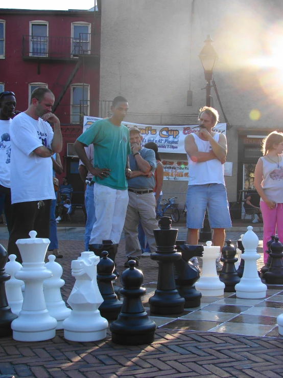 a group of people stand around a giant chess set