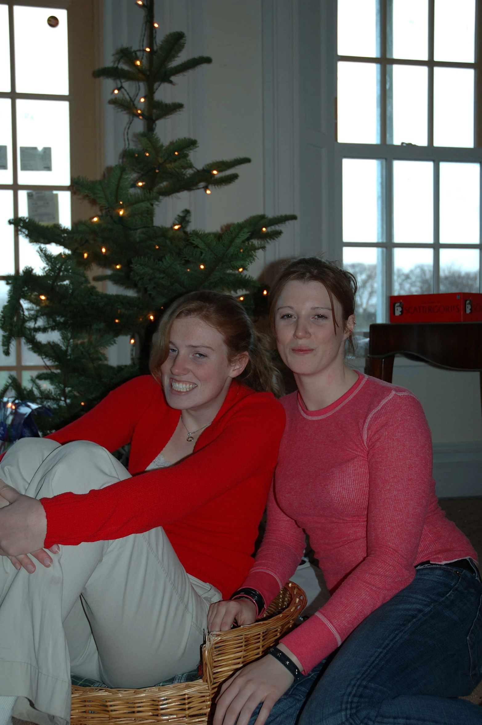 two woman sitting on the floor and posing for a po in front of a christmas tree