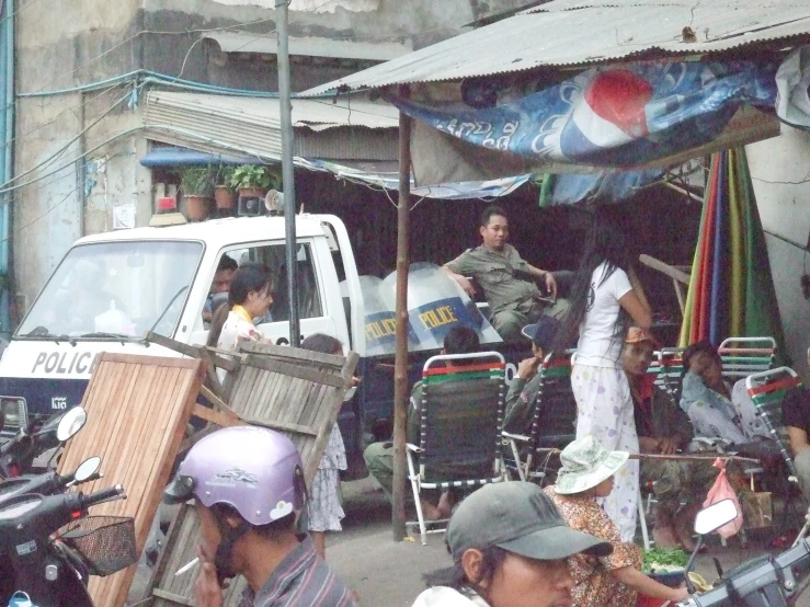 a group of people sitting and standing around a small tent on the street