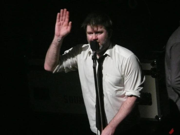 a person in white shirt and tie holding his hand up to say soing