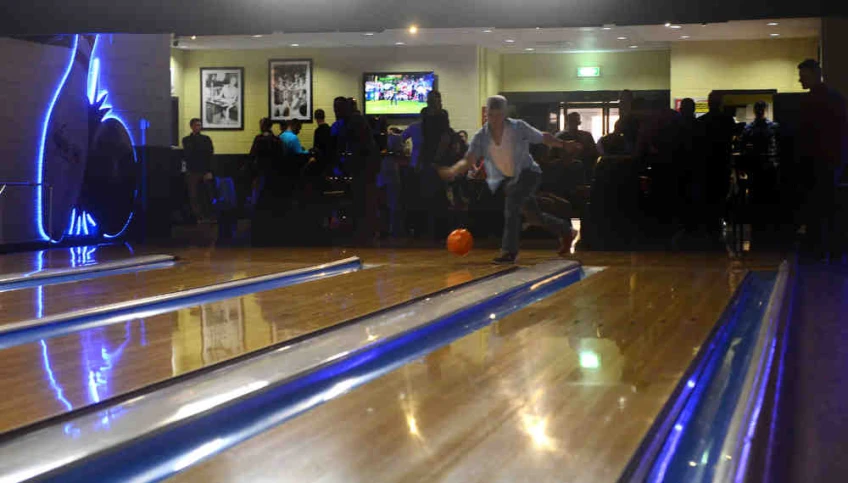 several bowling lanes with people watching and watching them play