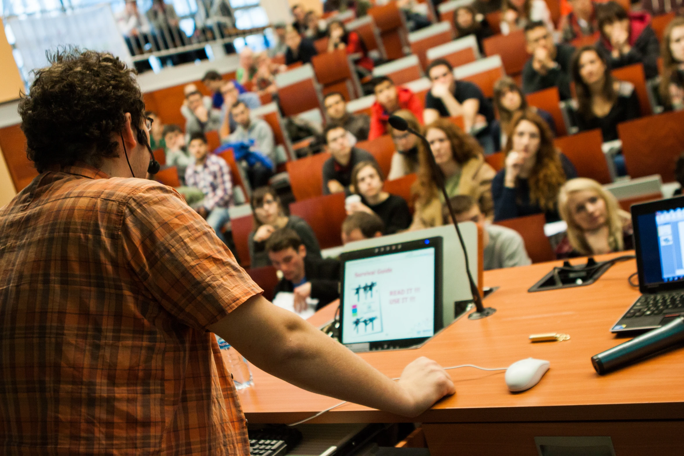 a man in an auditorium speaking with a laptop