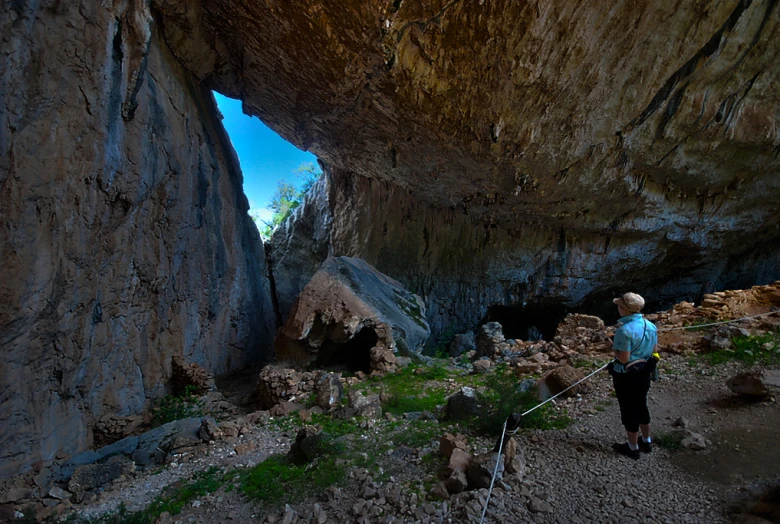 the man stands near the huge rock with his dog