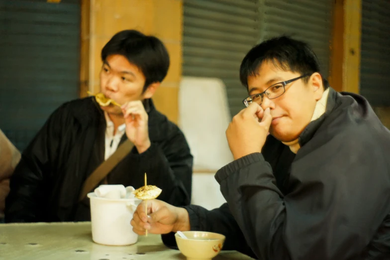 a man eating food from a white bowl while another man in black holds a spoon