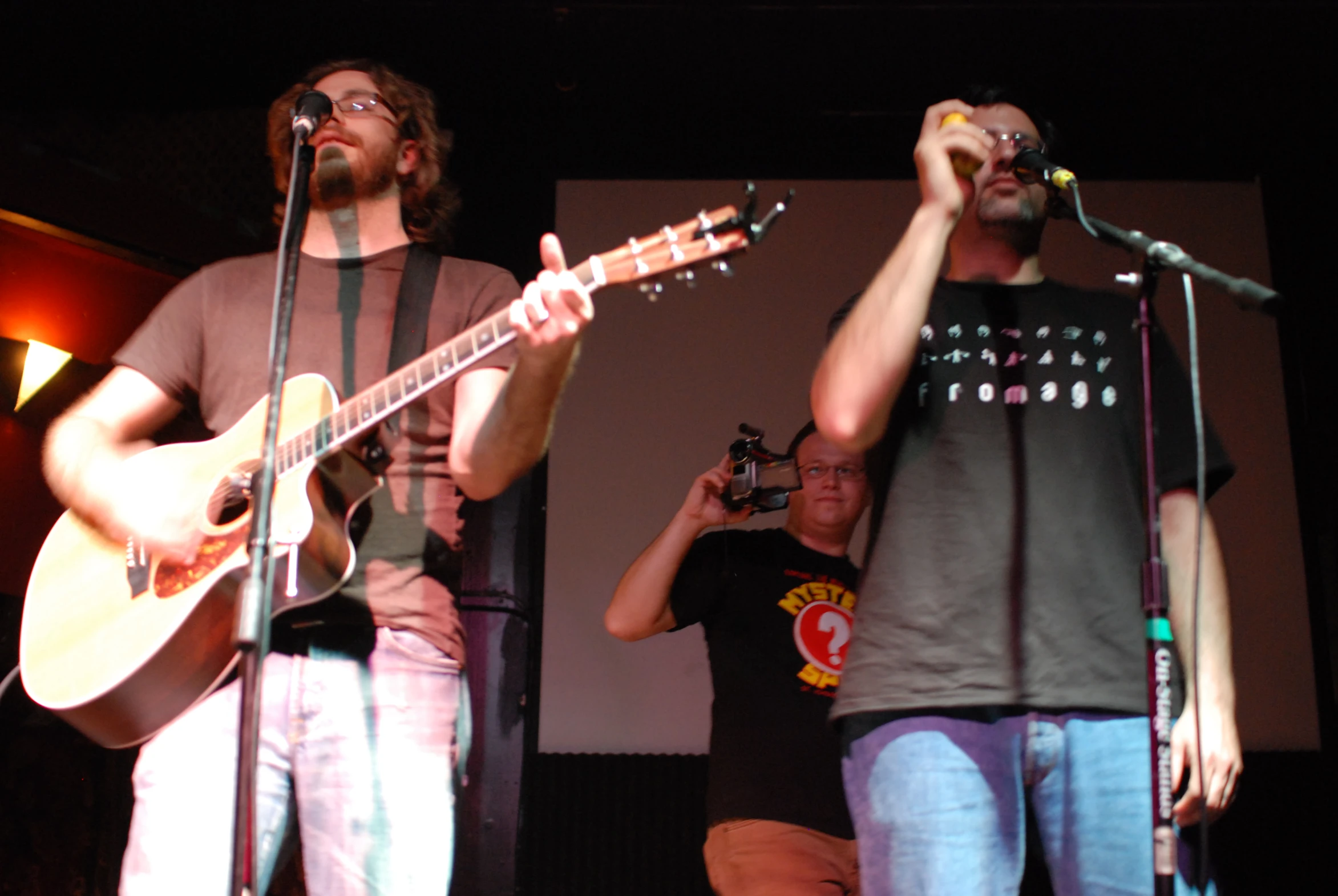 three musicians perform at a concert while one holds his guitar