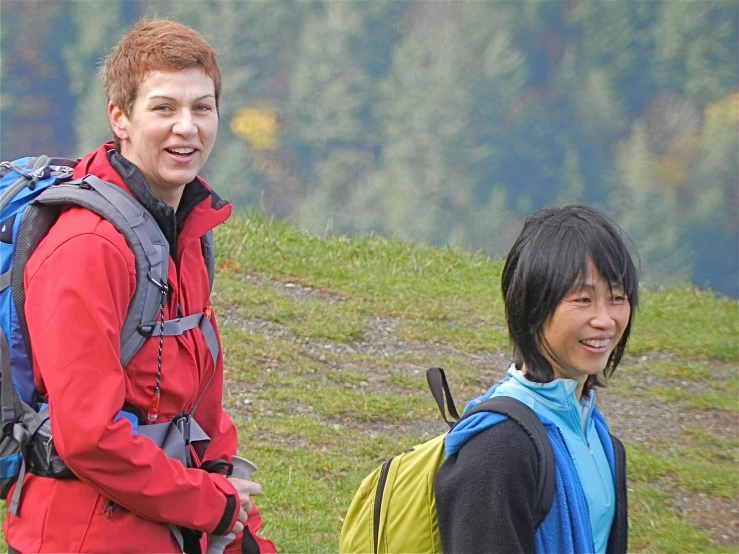 two smiling hikers on a hillside near a forest