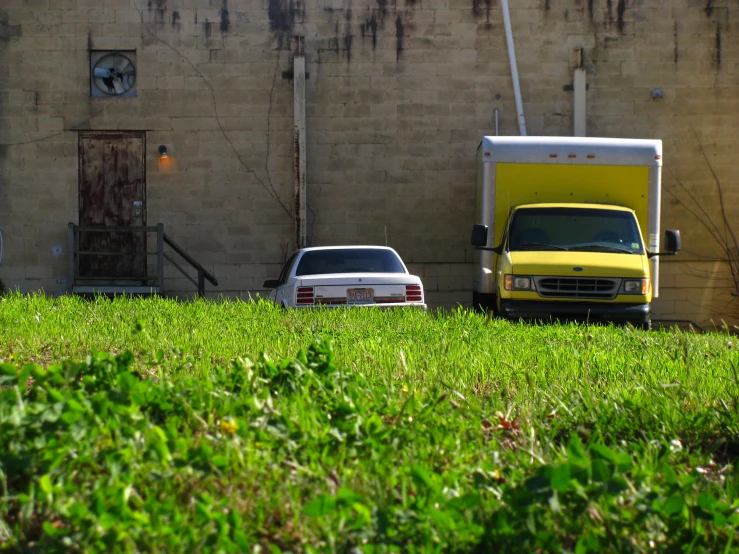 a yellow truck sitting by a building and another vehicle in the grass
