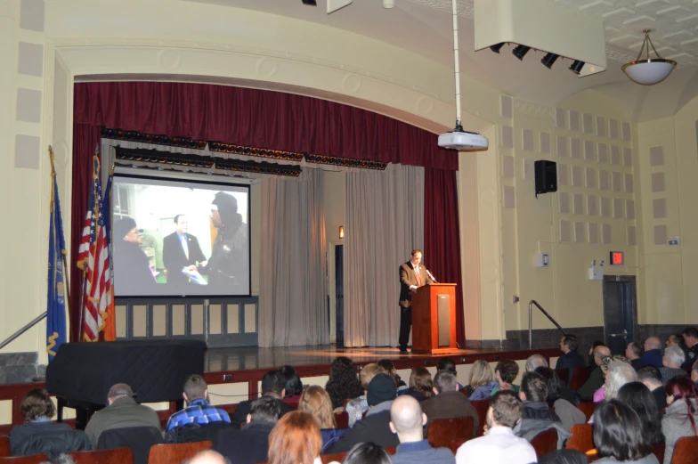 audience watching politician on screen in large auditorium