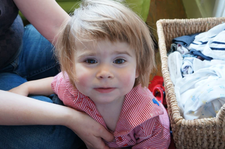 small toddler sitting next to basket with folded clothing