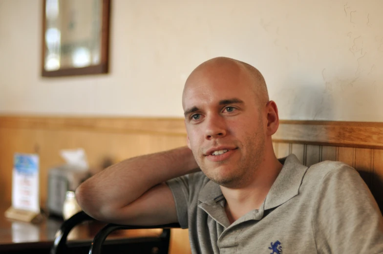 a man sits in a chair smiling with his head resting on the wall