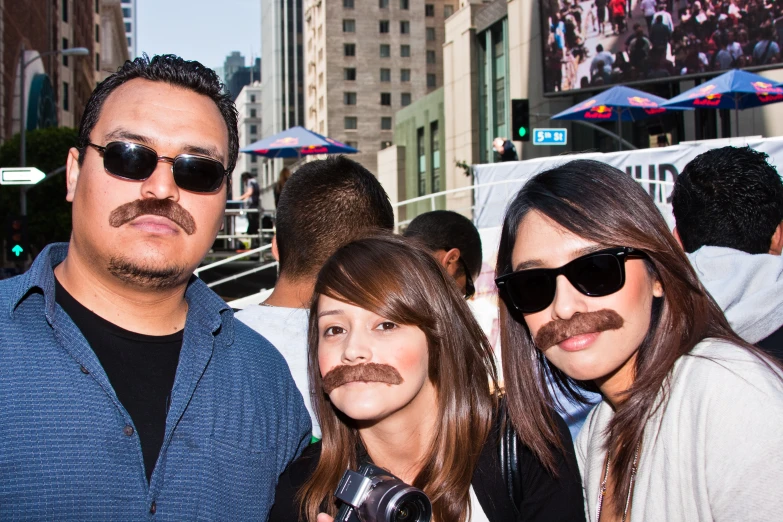 two woman and a man with fake mustaches on a busy street