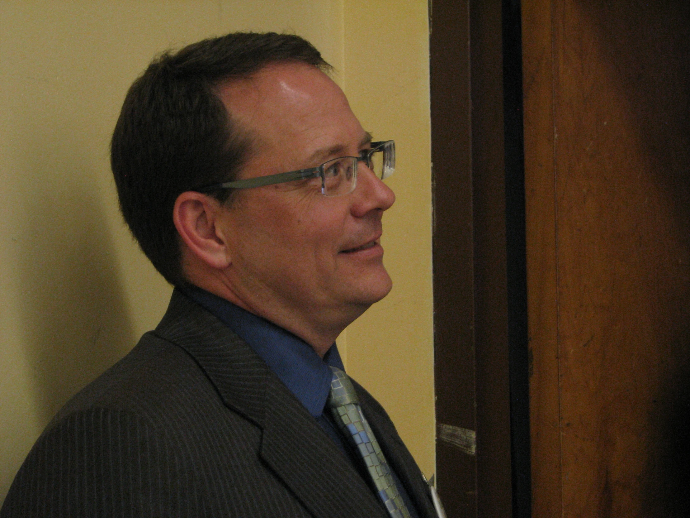a man wearing a tie and glasses standing next to a door