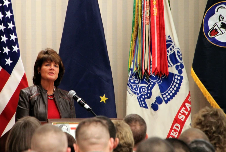 a woman stands in front of a microphone as others watch