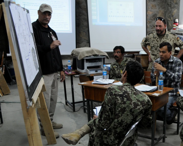 a man stands in front of his class with a class in the background