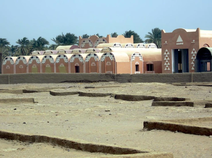 a desert scene with several adobe buildings, desert landscape and green trees in the background