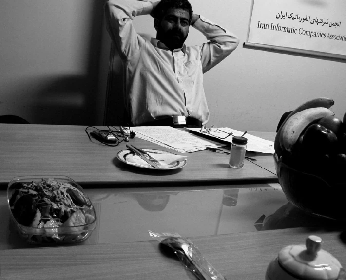 a man in white shirt sitting at desk with his hands on his ears