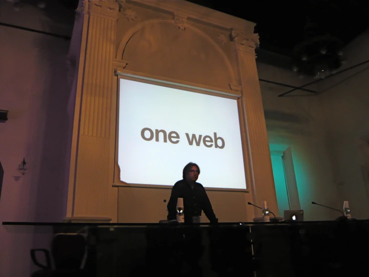 a man stands in front of an enormous sign that says one web