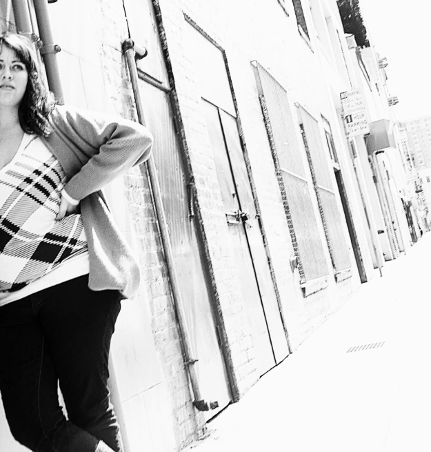 a beautiful young woman leaning against the side of a wall