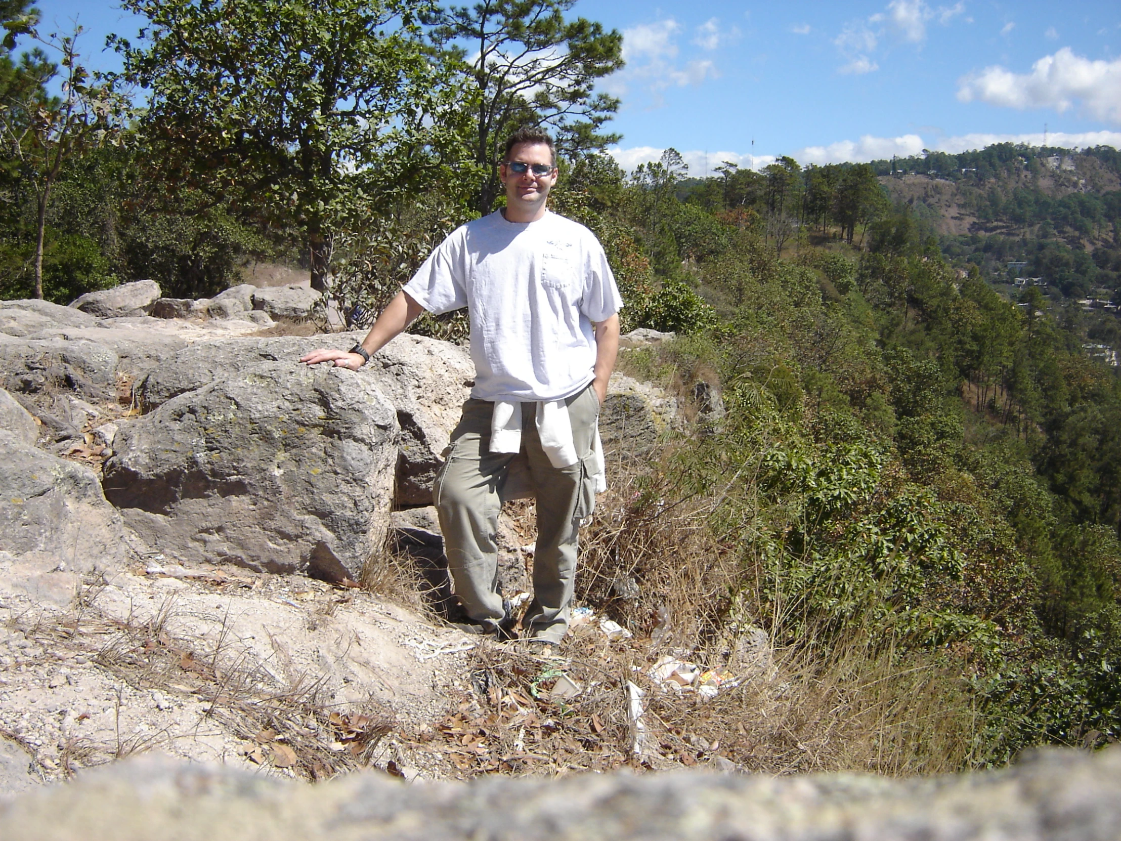 a man in white shirt and khaki pants standing on top of rocks