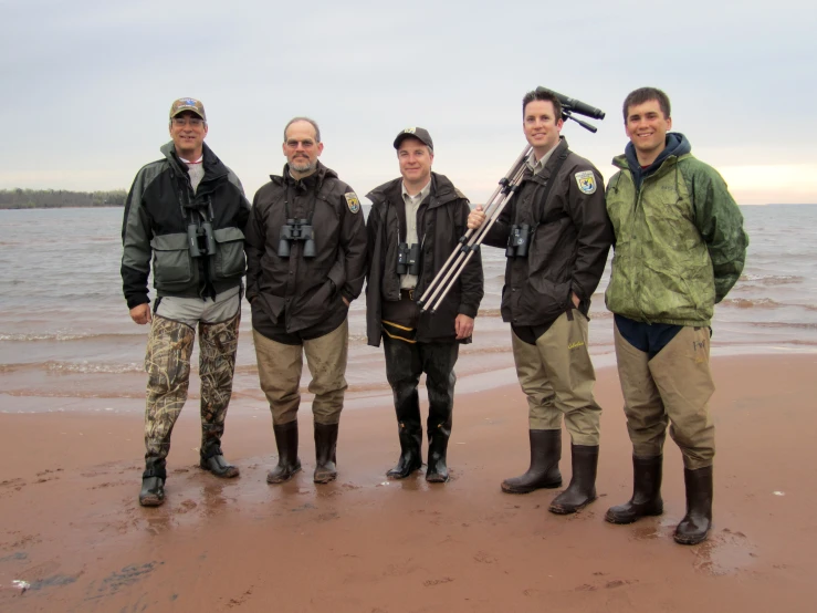 several people are standing on the beach wearing rain boots