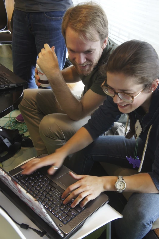 a woman is working on a computer while another man stands over her