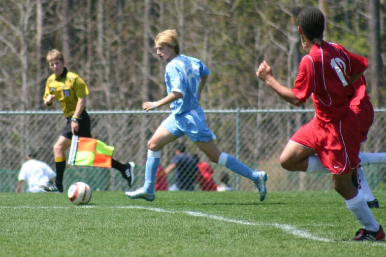 three boys are playing soccer and one is running after the ball