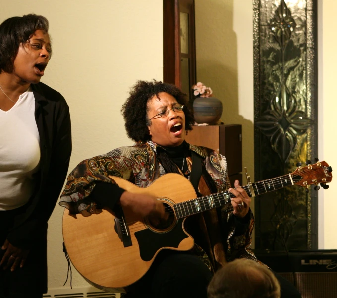 a woman with an acoustic guitar sings while another woman looks on