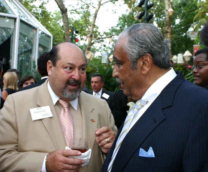 two men talking and drinking wine in a crowd