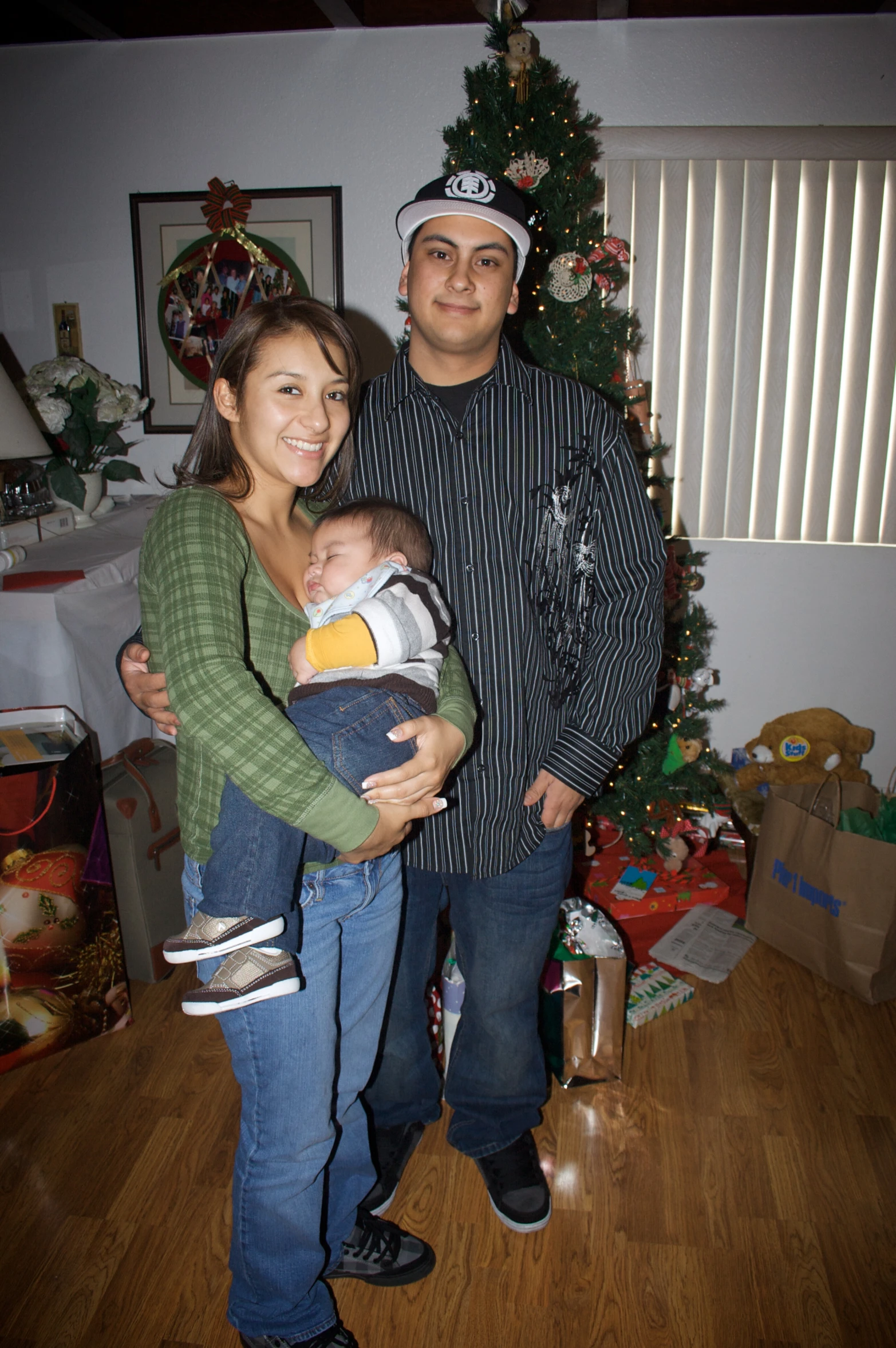 a couple with a baby pose for the camera near a christmas tree