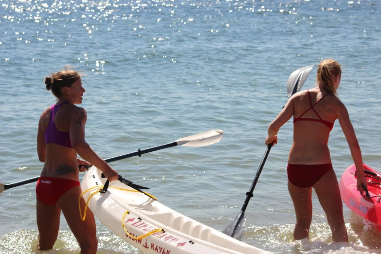 two women in a bikinis hold paddles to surf