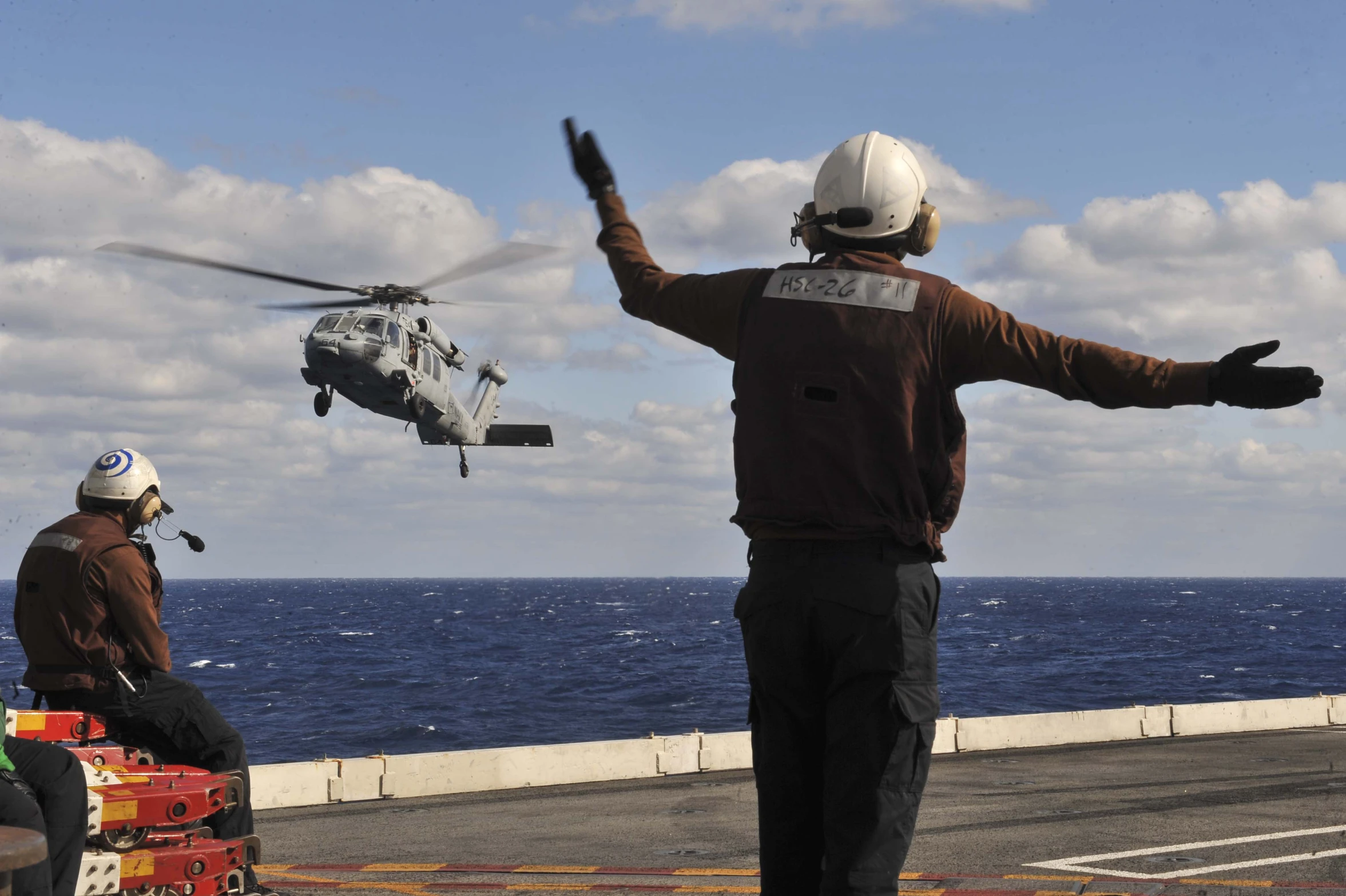 two people stand on the deck with a helicopter and rescue worker