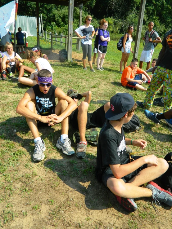 a group of s sit together on a grassy area while adults watch